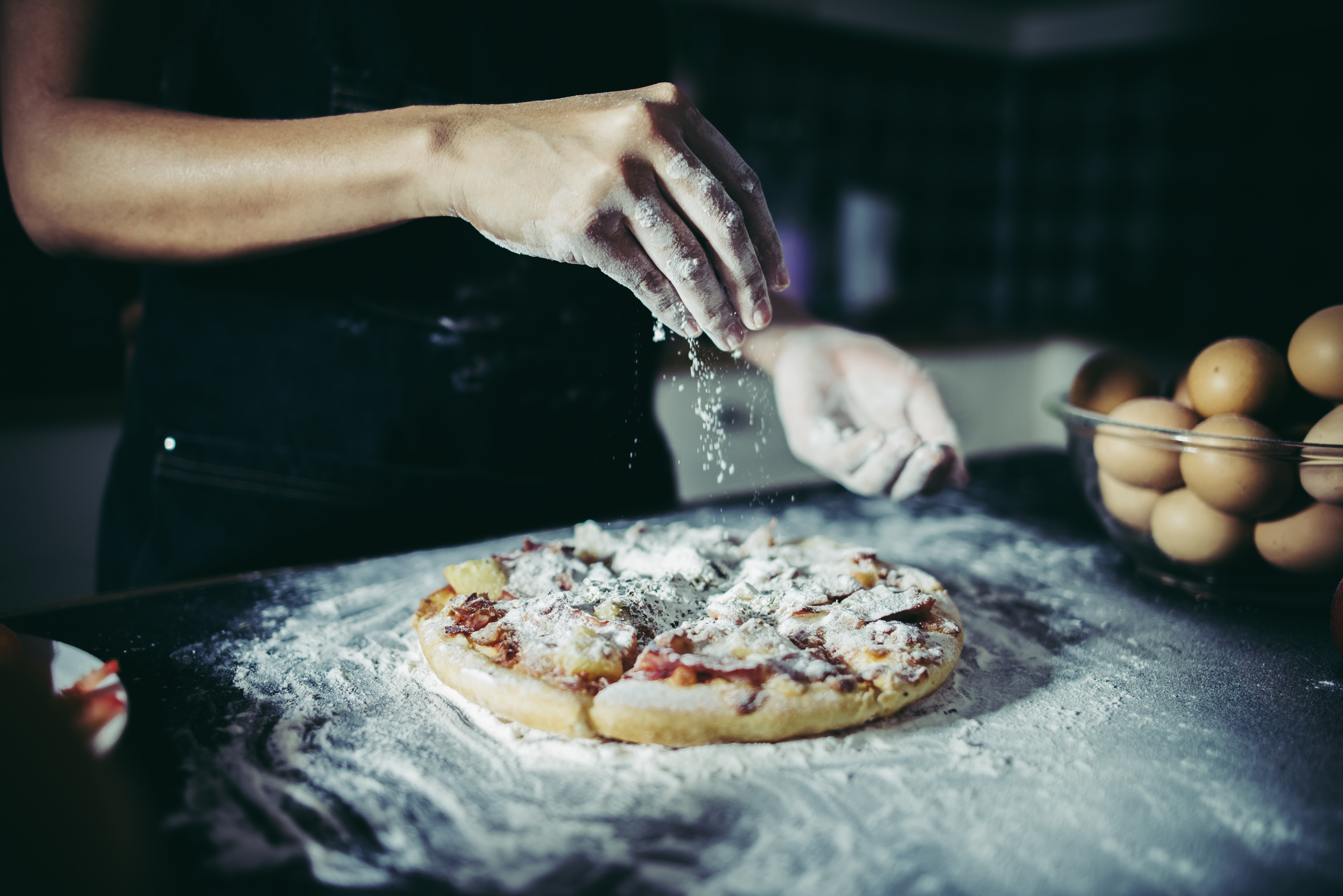 Chef sprinkling flour over raw pizza dough during preparation.