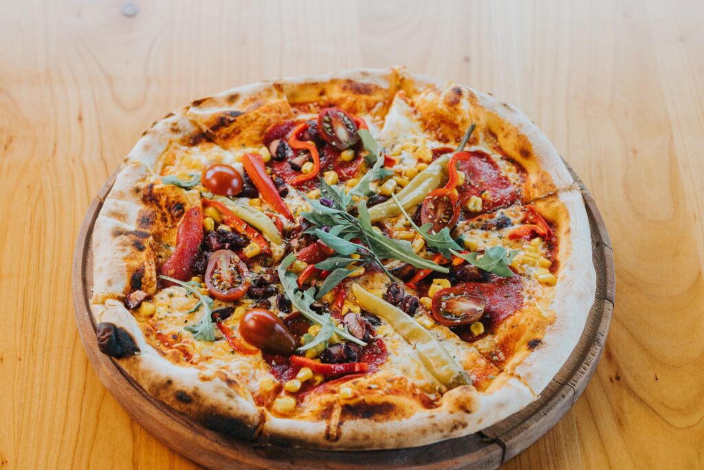 Close-up of a loaded pizza topped with veggies on a wooden serving board at Manny and Olga’s.