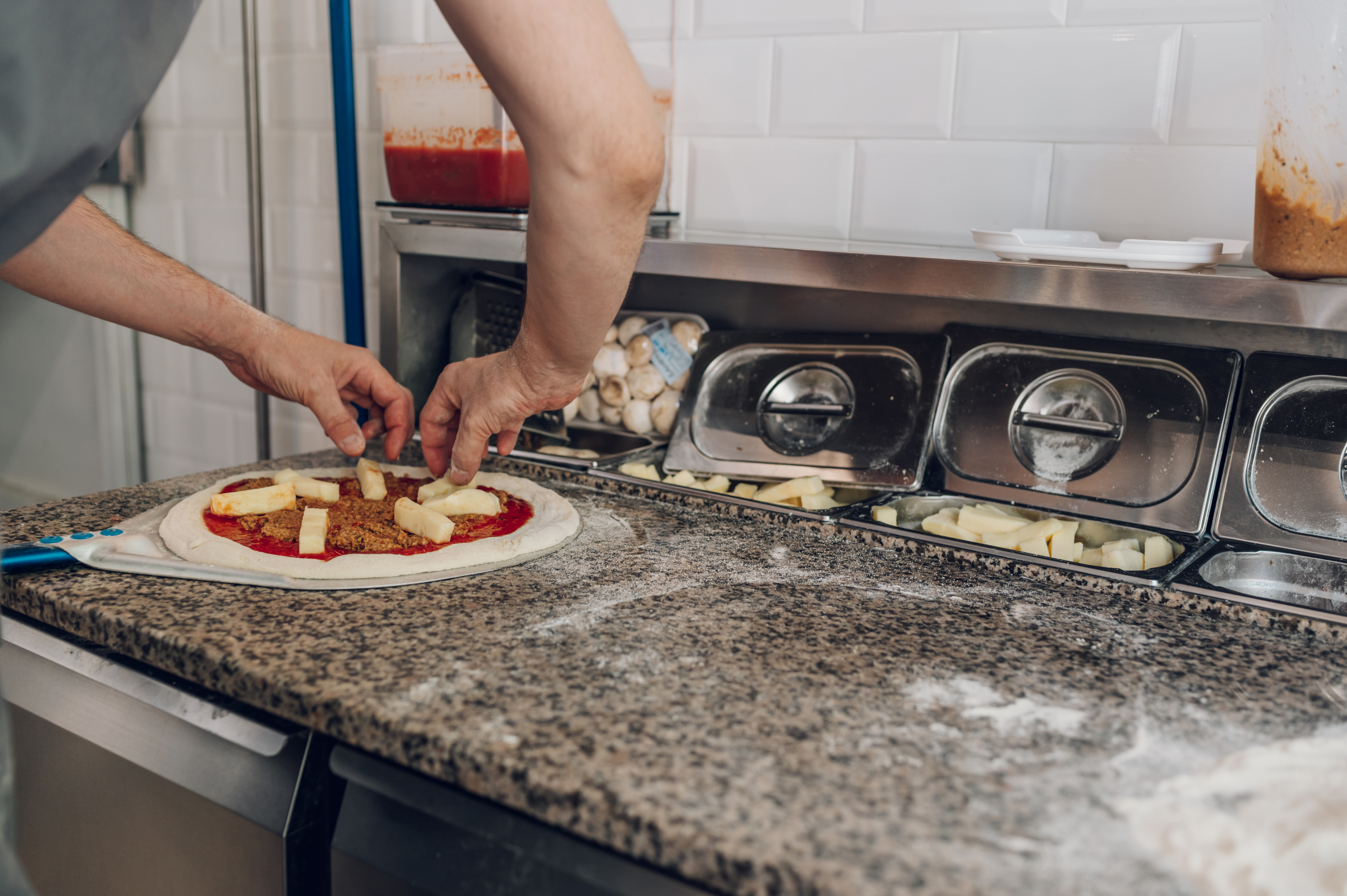 Chef adding toppings to a pizza before baking in a restaurant kitchen.