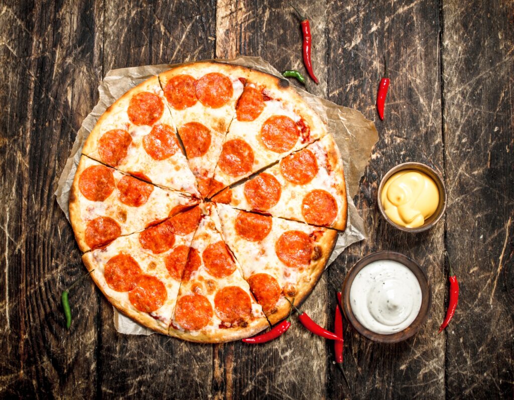Manny and Olga’s pepperoni pizza on a parchment, with sauces and chilli on a rustic table.