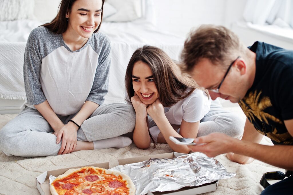 Manny and Olga’s pizza shared by a smiling dad and daughters, during a cozy movie night.