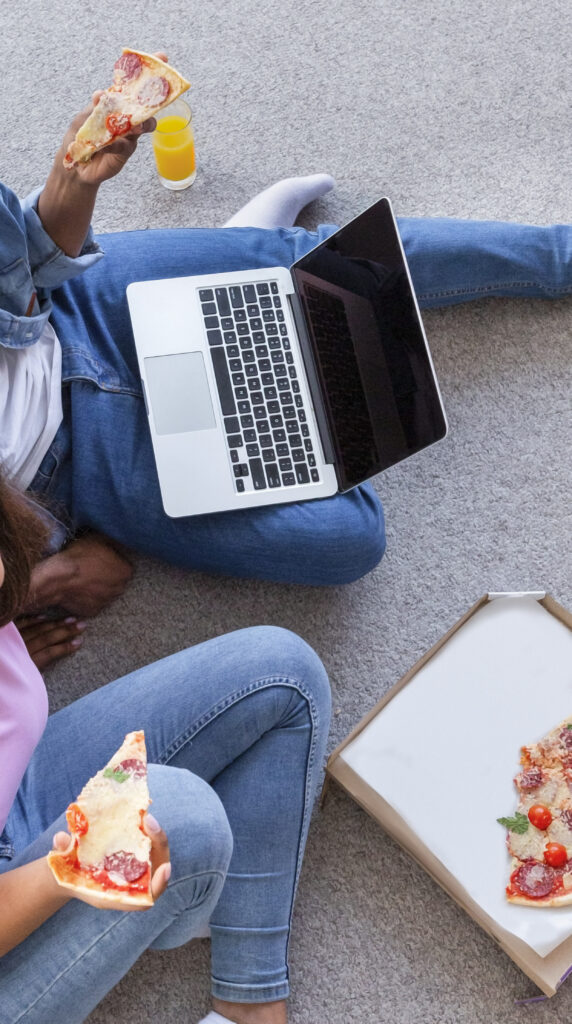 African couple enjoying pizza while streaming a movie on a laptop, representing cozy Netflix night.