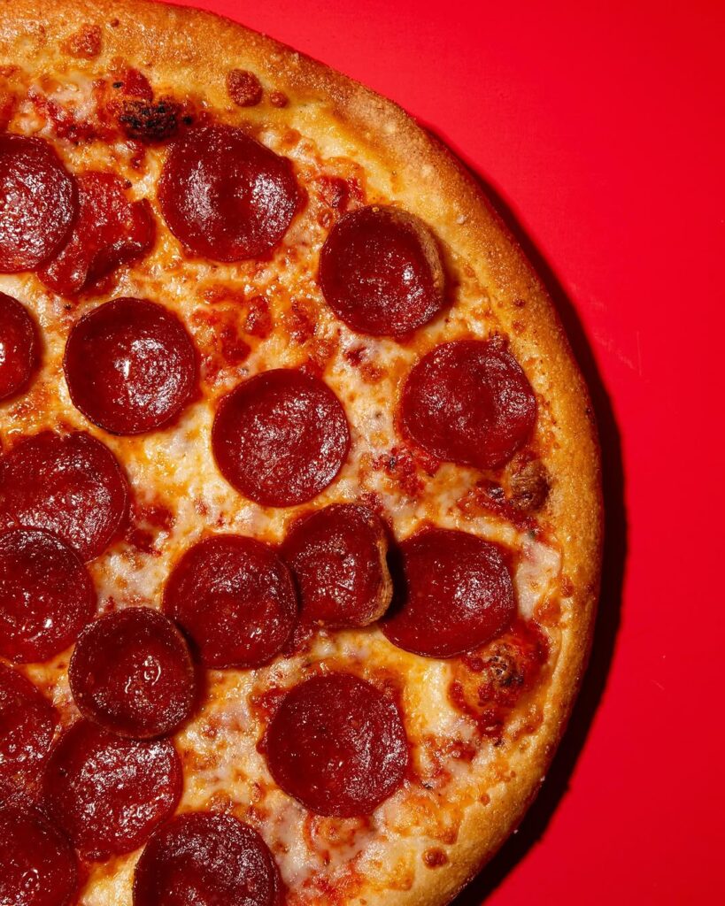 Close-up of pepperoni pizza from Manny & Olga’s on a red background.