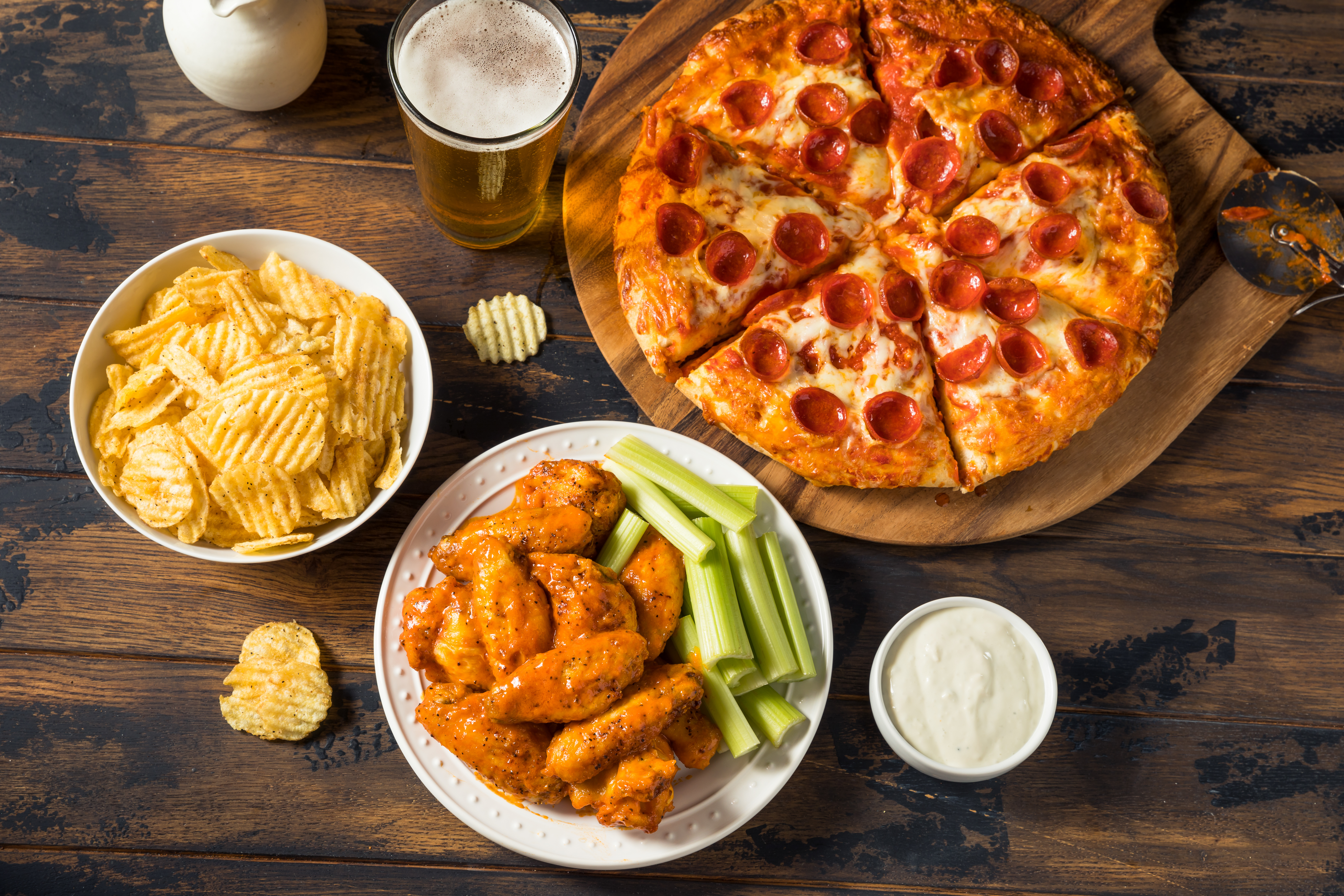 Pepperoni pizza served with buffalo wings and a glass of soda on a wooden table.