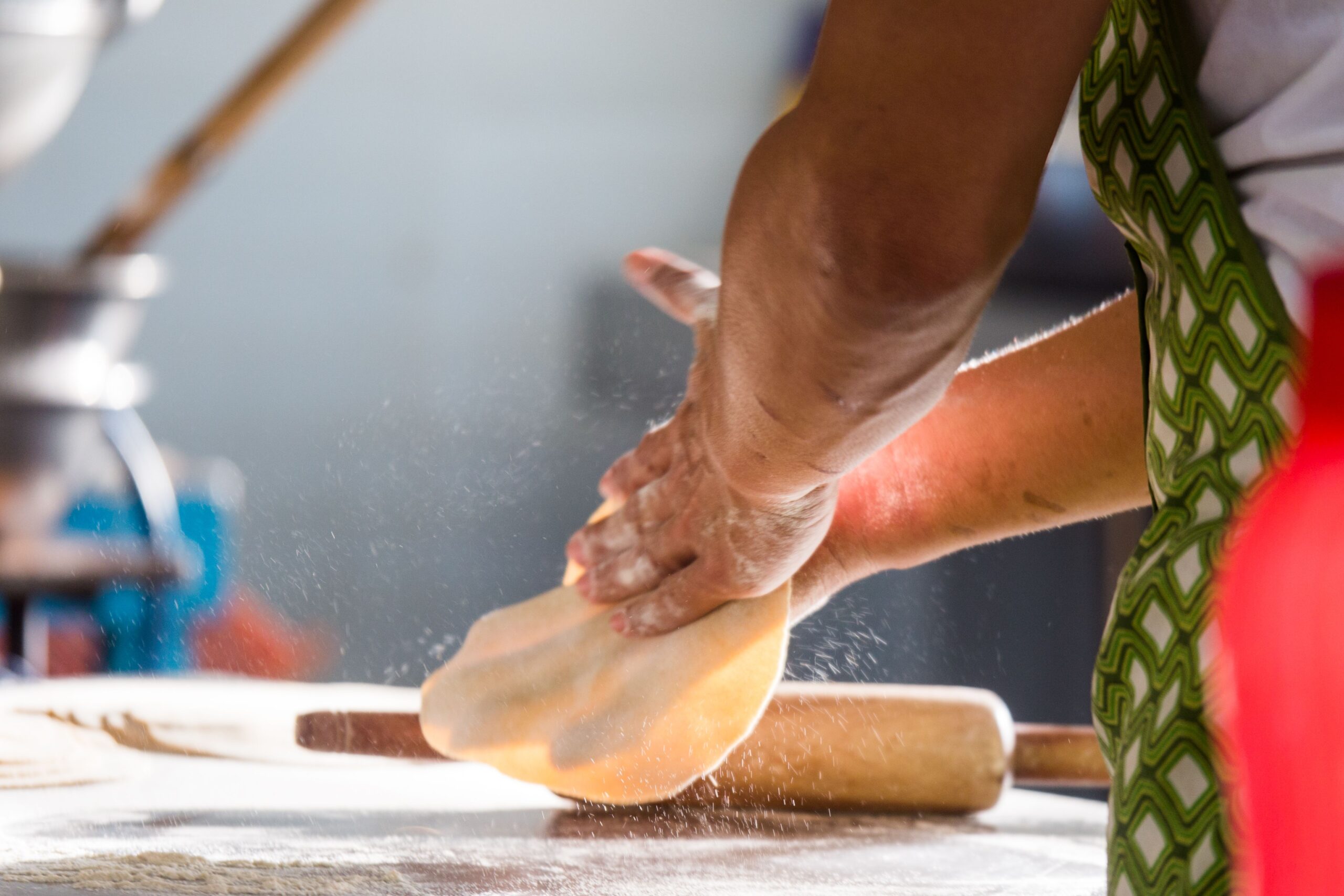 Person stretching fresh pizza dough by hand on a floured surface with a rolling pin nearby.
