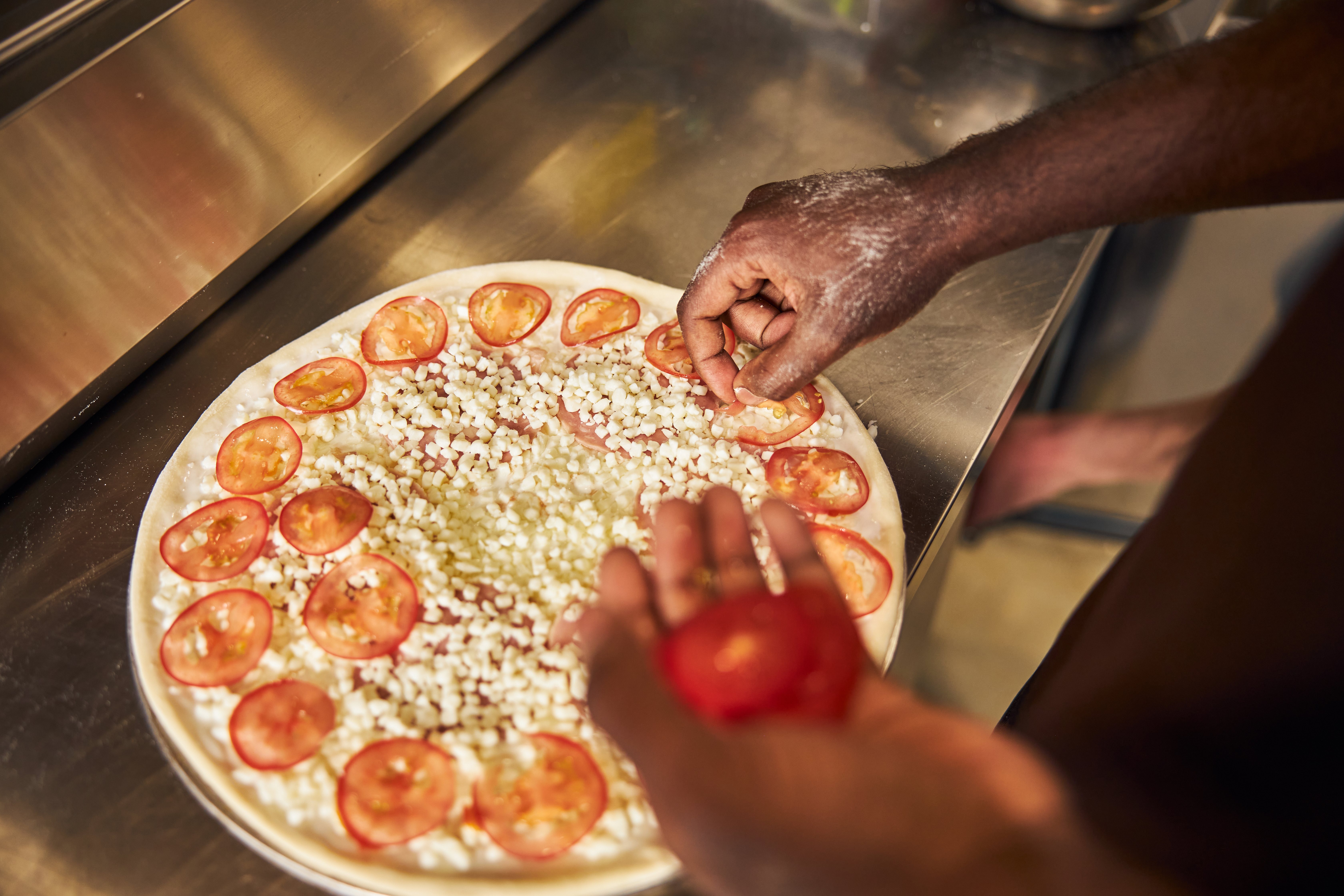 Person placing tomato slices on pizza dough before baking.