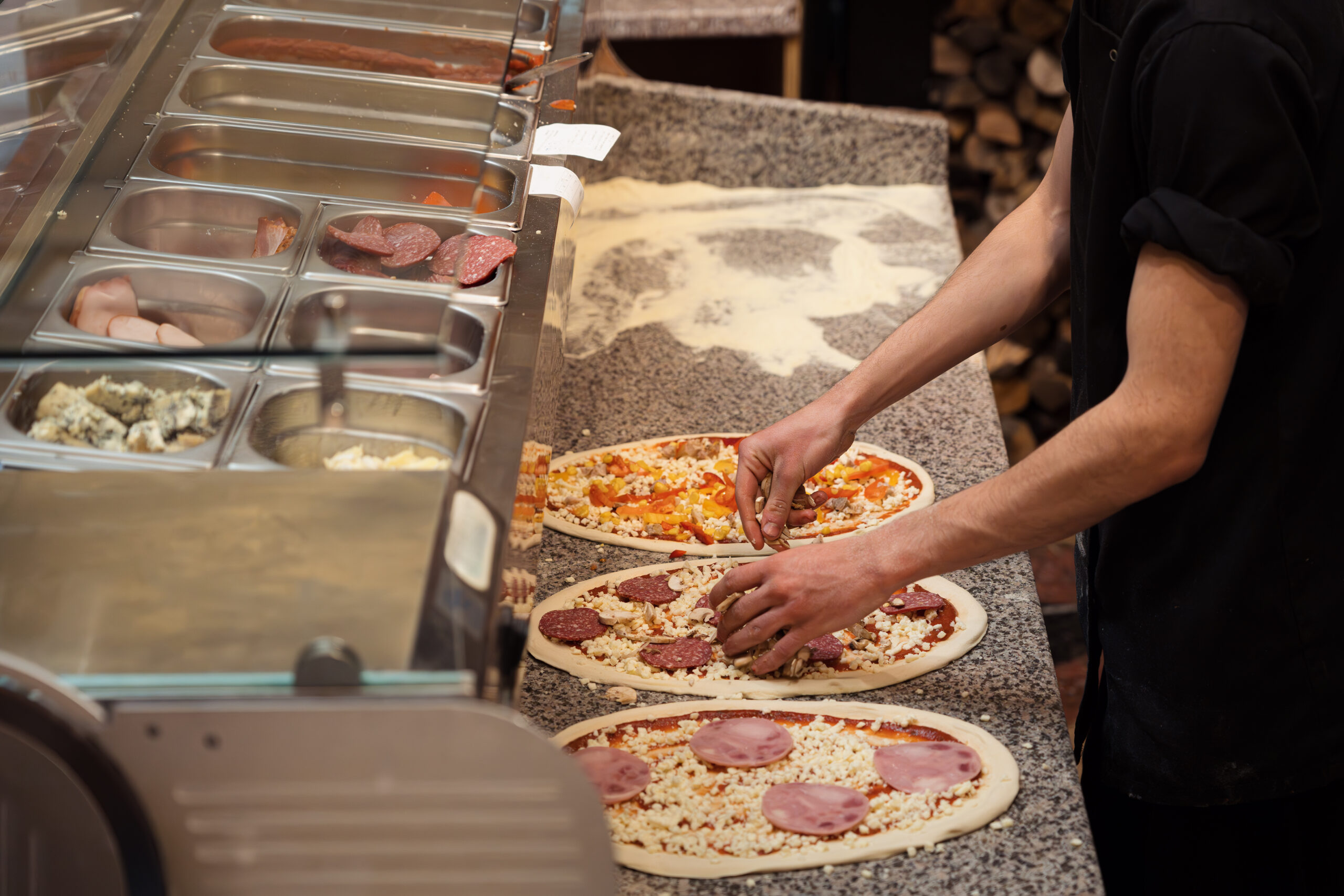 Chef preparing fresh pizzas with toppings at Manny & Olga’s kitchen counter.