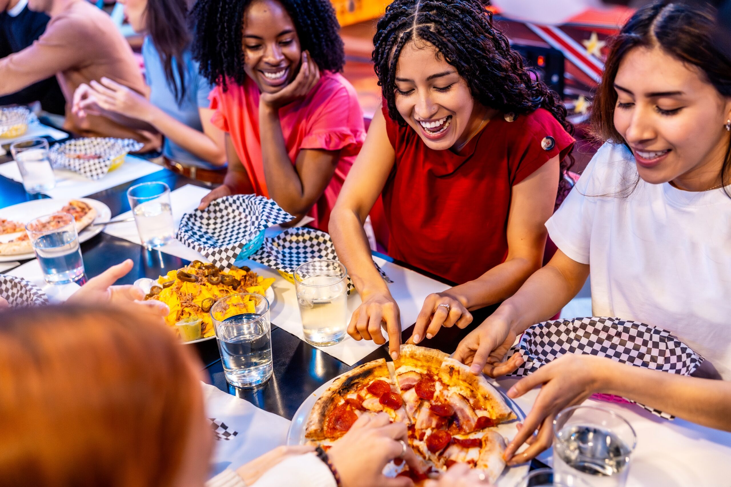 Friends laughing and sharing pizza together at a neighborhood pizzeria table.