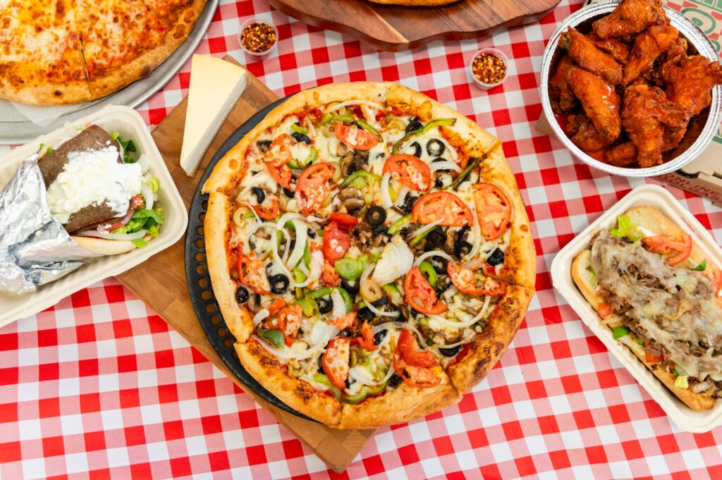 Manny and Olga’s veggie pizza topped with tomatoes, olives, onions, and peppers, served with wings and subs.