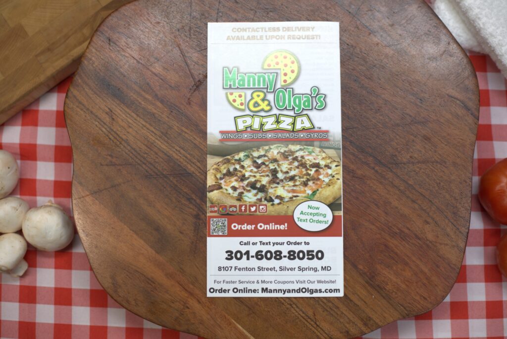 Manny and Olga’s Pizza flyer on a wooden board with contact details and online ordering information displayed..