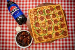 Manny and Olga’s square pepperoni and green pepper pizza served with wings and a bottle of Pepsi.