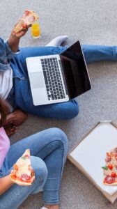 African couple watching a movie on a laptop while eating pizza at home.