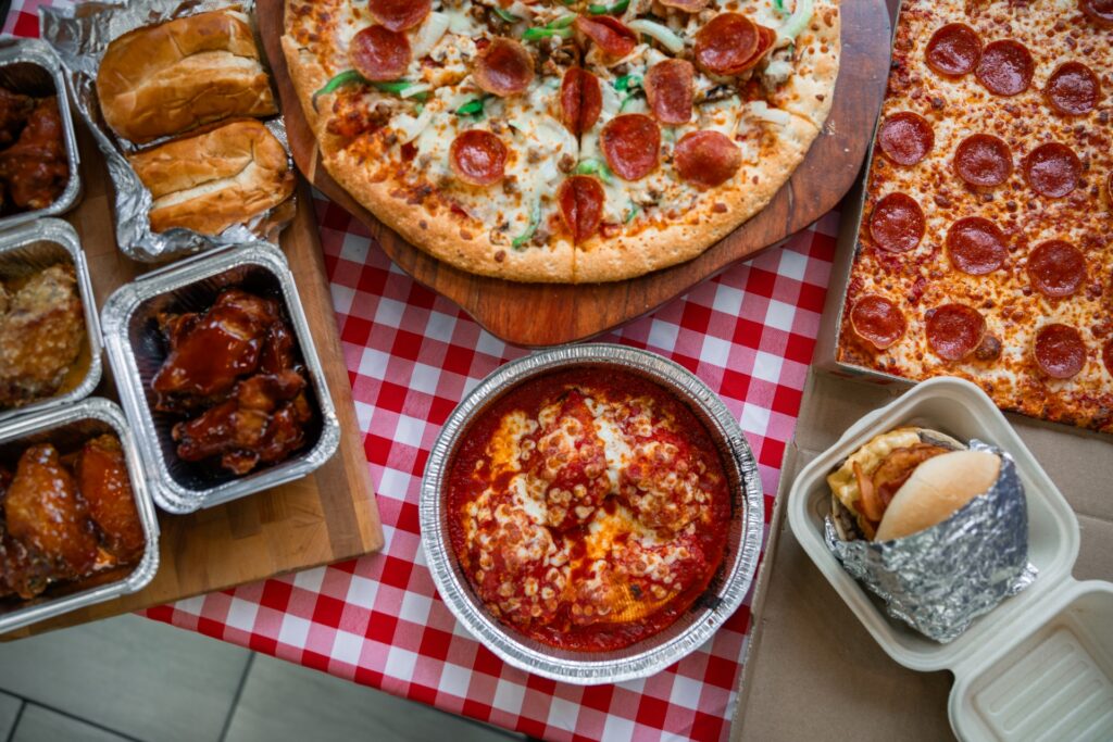 Assorted Manny & Olga’s party spread with pizza, wings, subs, and pasta trays for D.C. catering events.