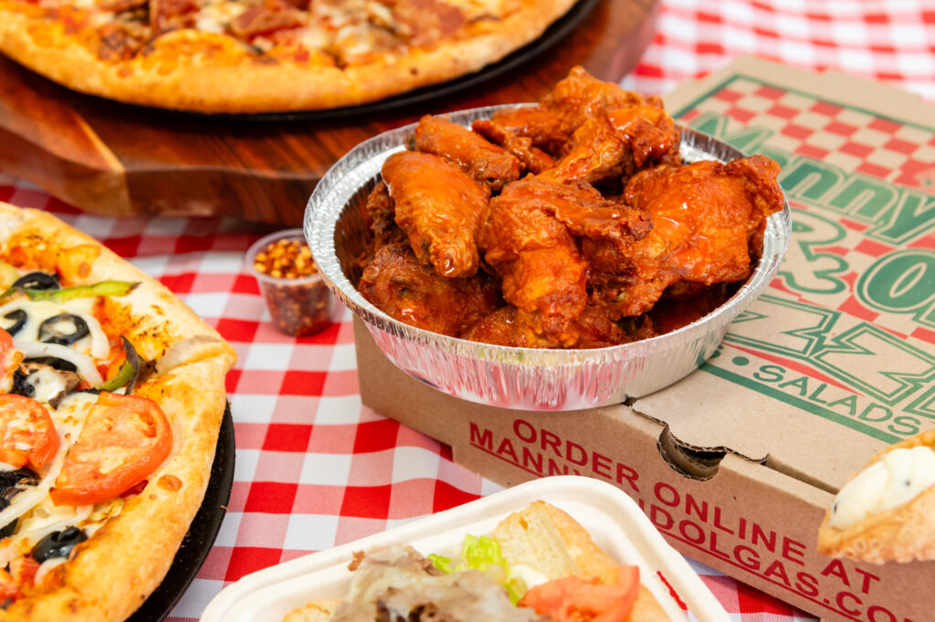 Manny & Olga’s buffalo wings and pizzas on a red checkered table with a branded pizza box.