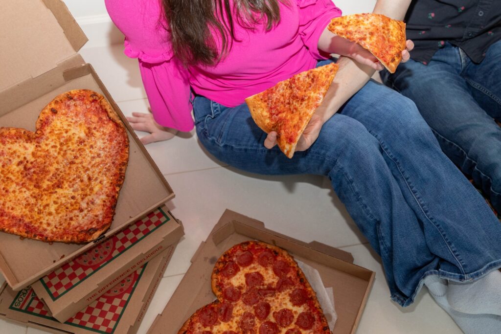 Couple sharing heart-shaped pizza slices from Manny & Olga’s Pizza during Valentine’s night in.