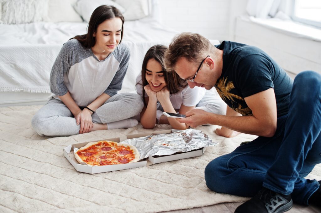 Manny and Olga’s pizza shared by a smiling dad and daughters, during a cozy movie night.