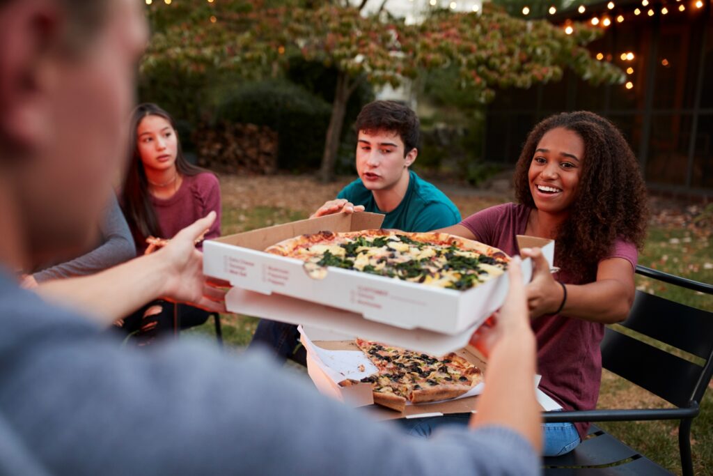Father receives Manny and Olga’s pizza from the kids during a joyful outdoor celebration.