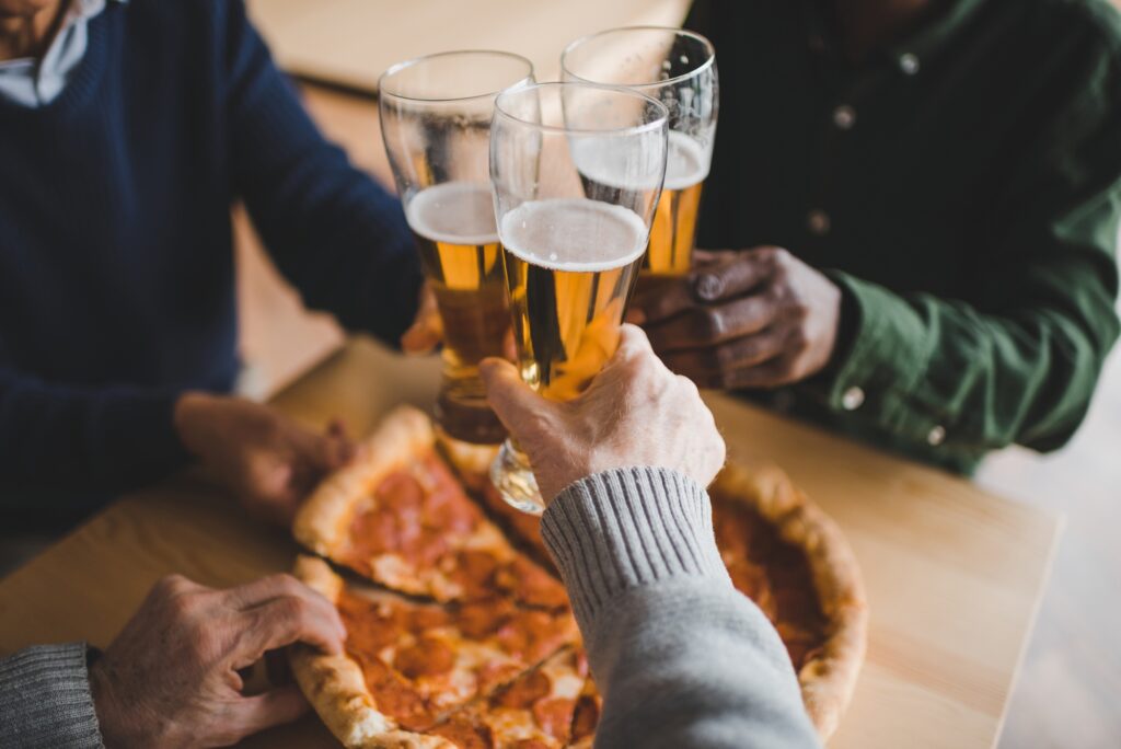 Three friends toast with beer and a meat pizza.