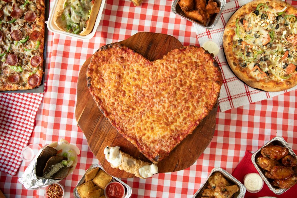 A heart-shaped Valentine’s pizza from Manny & Olga’s Pizza surrounded by wings, sides, and specialty pies.