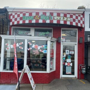 Manny & Olga’s Pizza storefront with red brick exterior.