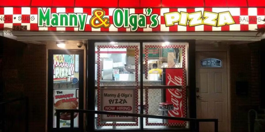 The entrance to Manny & Olga's Pizza shop with a well-lit banner.