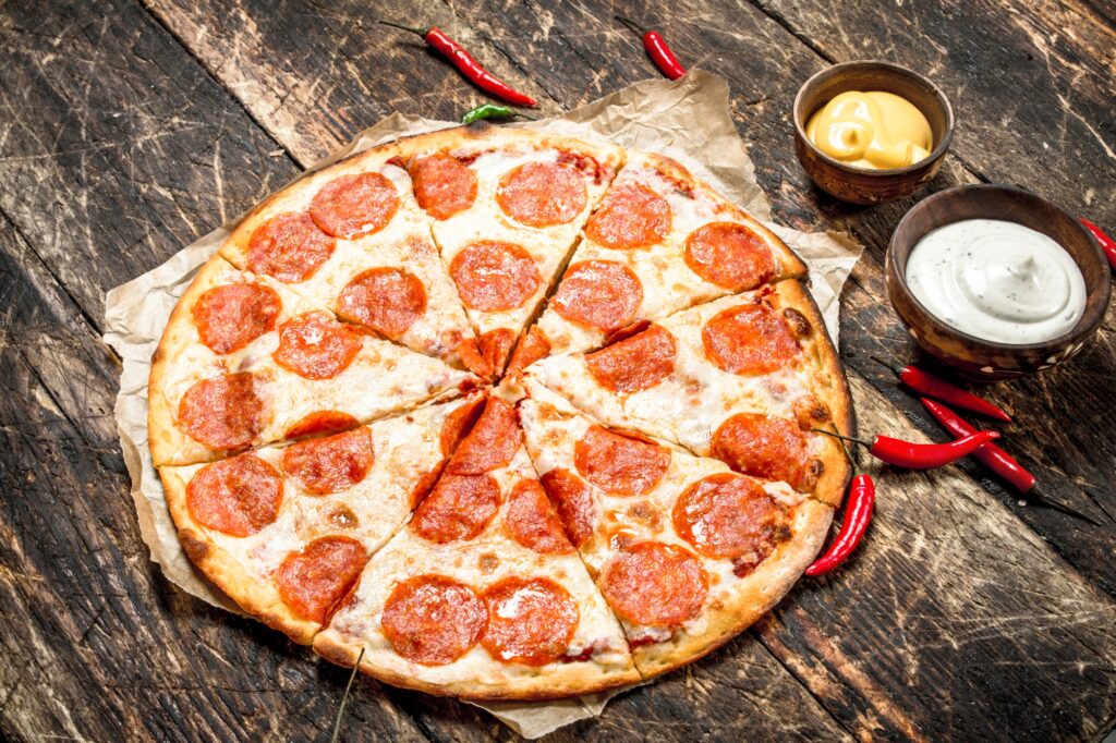 Manny and Olga’s pepperoni pizza on a parchment, with sauces and chilli on a rustic table.