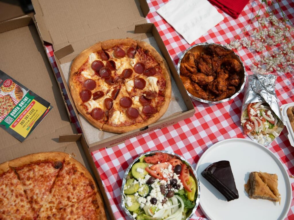 A picnic spread featuring hot, cheesy pizza, crispy wings, and hearty subs from Manny & Olga’s.