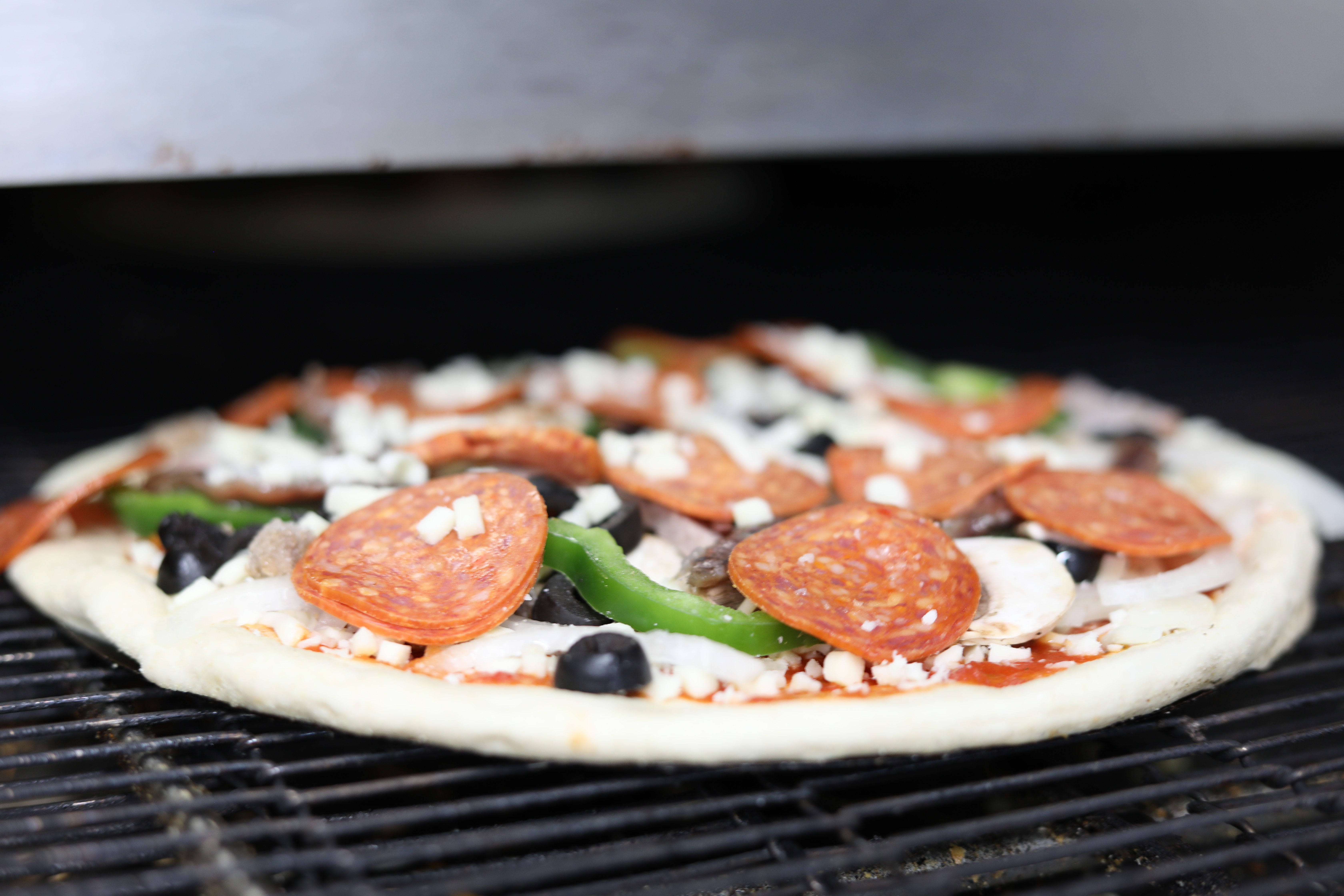 Manny & Olga’s pepperoni pizza with green peppers baking on an oven grate.