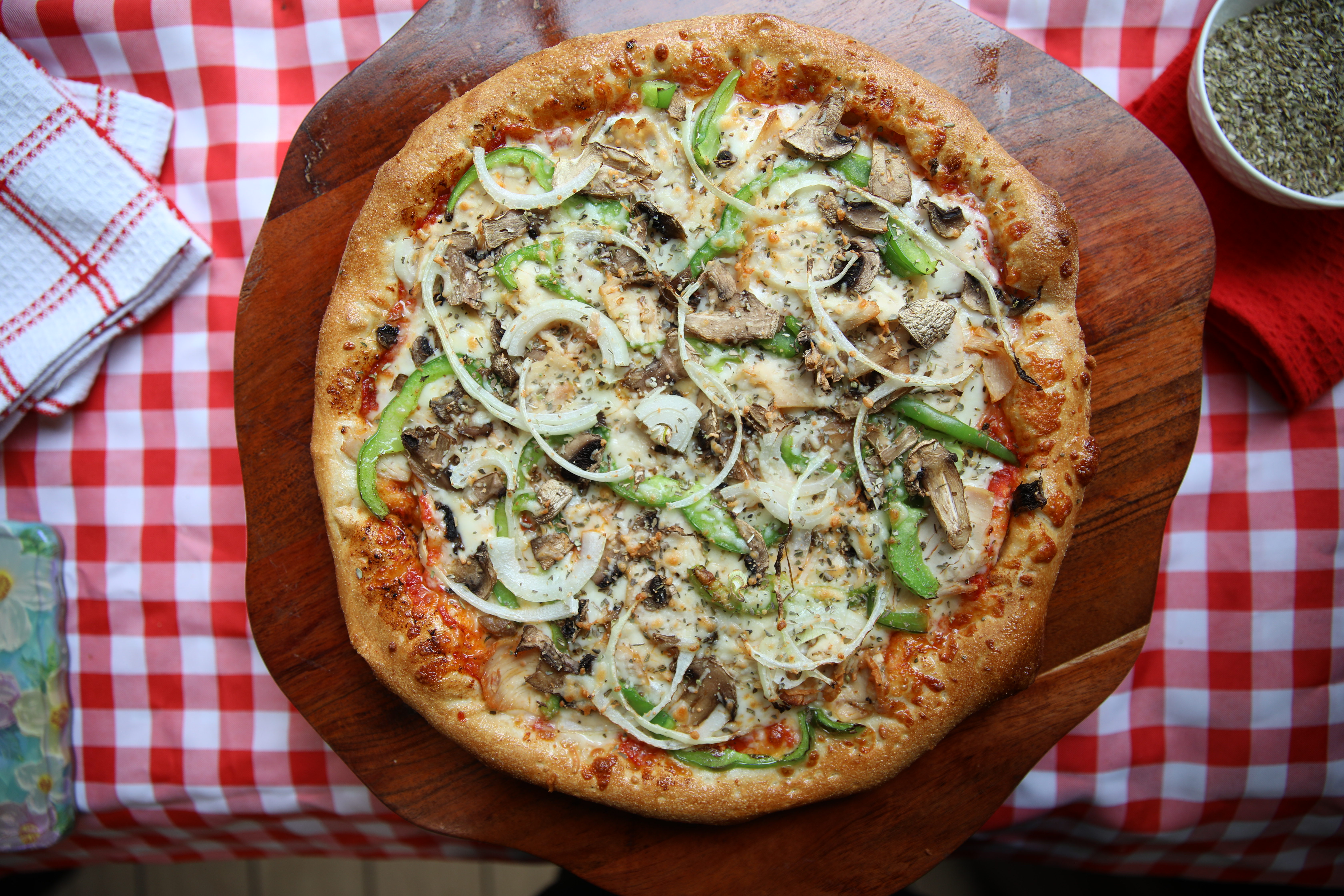 Manny & Olga’s vegetable pizza with onions, mushrooms, and green peppers on a wooden peel.