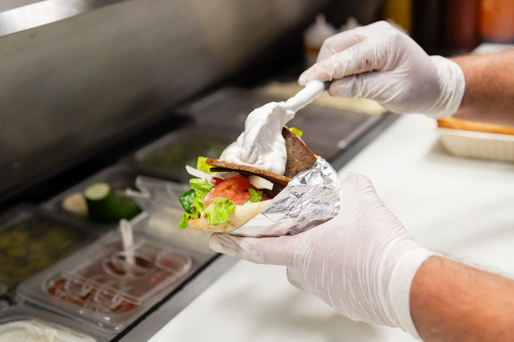Manny & Olga’s sub sandwich being filled with toppings and sauce.