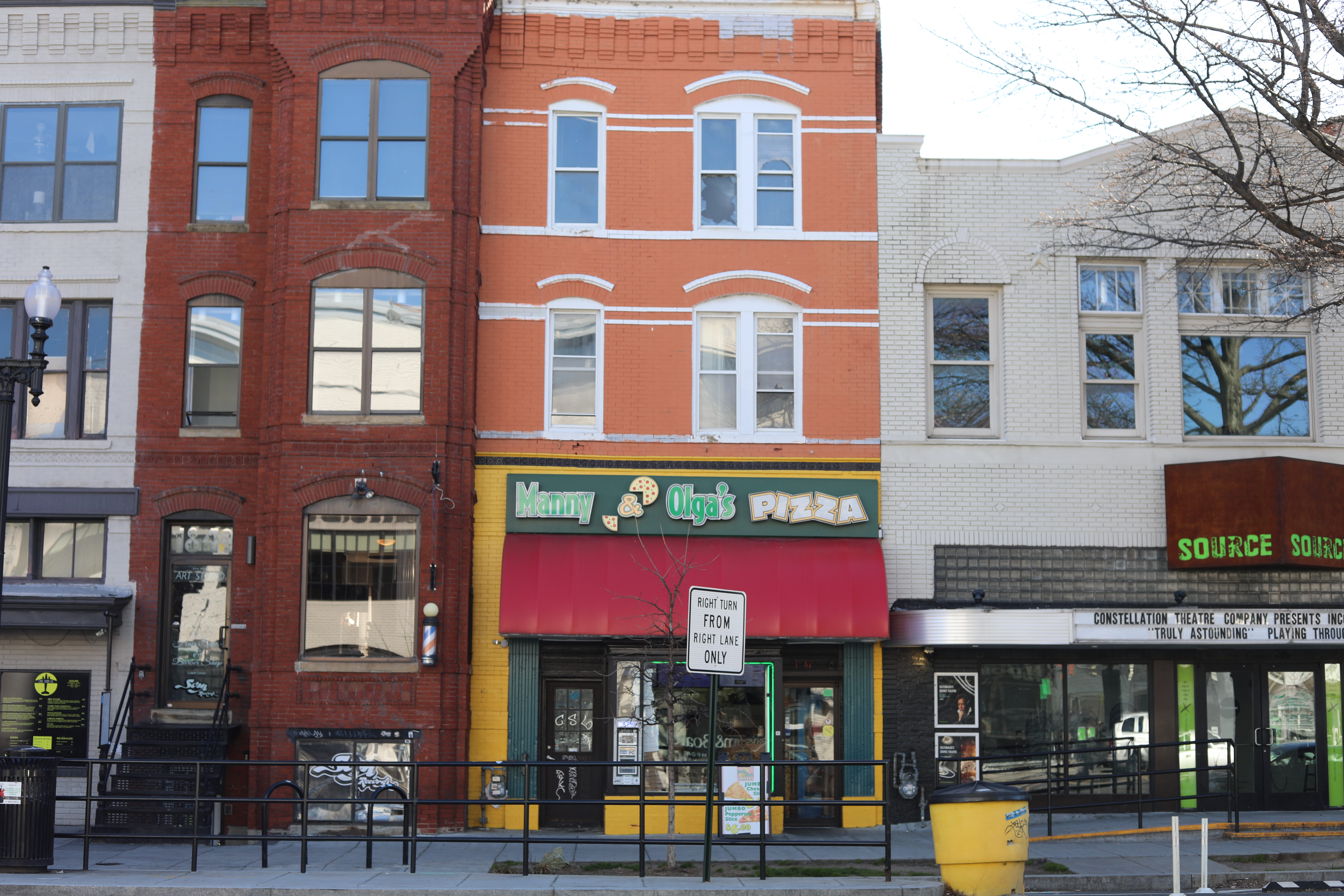 Manny & Olga’s Pizza storefront on 14th Street NW between two white buildings.