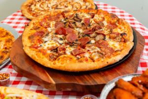 Meat-loaded pizza with pepperoni, sausage, and mushrooms served hot from Manny & Olga’s
