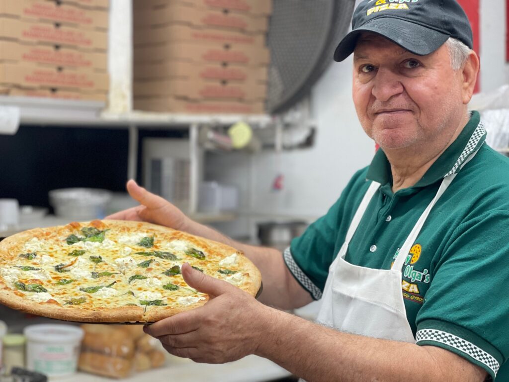 Team member holding a freshly baked pizza in the Manny & Olga’s kitchen