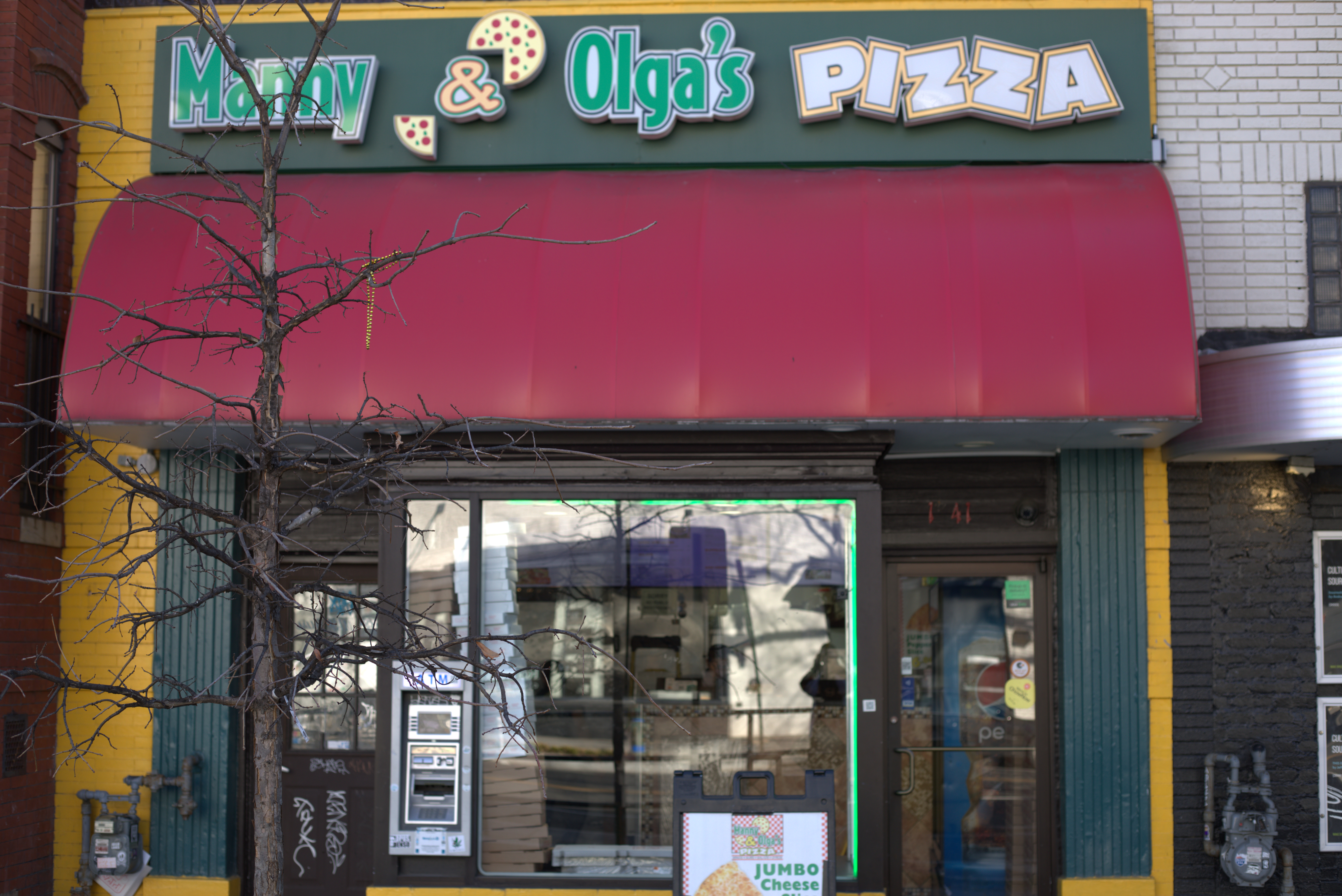 Manny & Olga’s Pizza restaurant on 14th Street with red awning, large windows, and daytime street view.