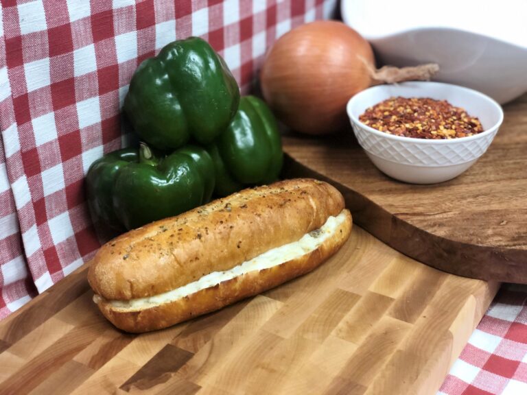 Golden garlic bread topped with melted cheese, served alongside fresh peppers, herbs, and seasonings on a rustic serving board.