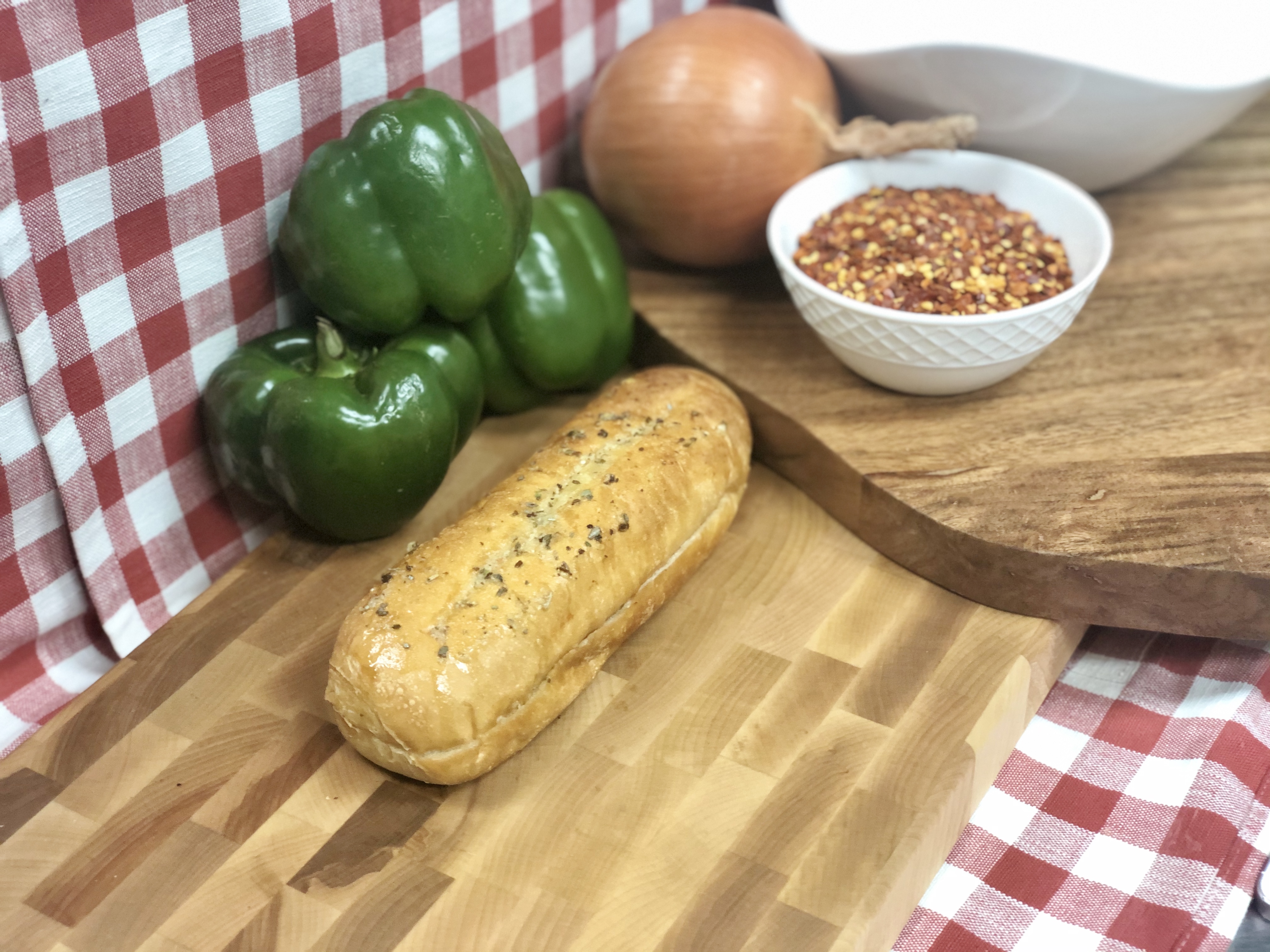 Freshly baked garlic bread displayed on a wooden board with sliced peppers, onions, and seasonings, highlighting a classic pizza side dish.