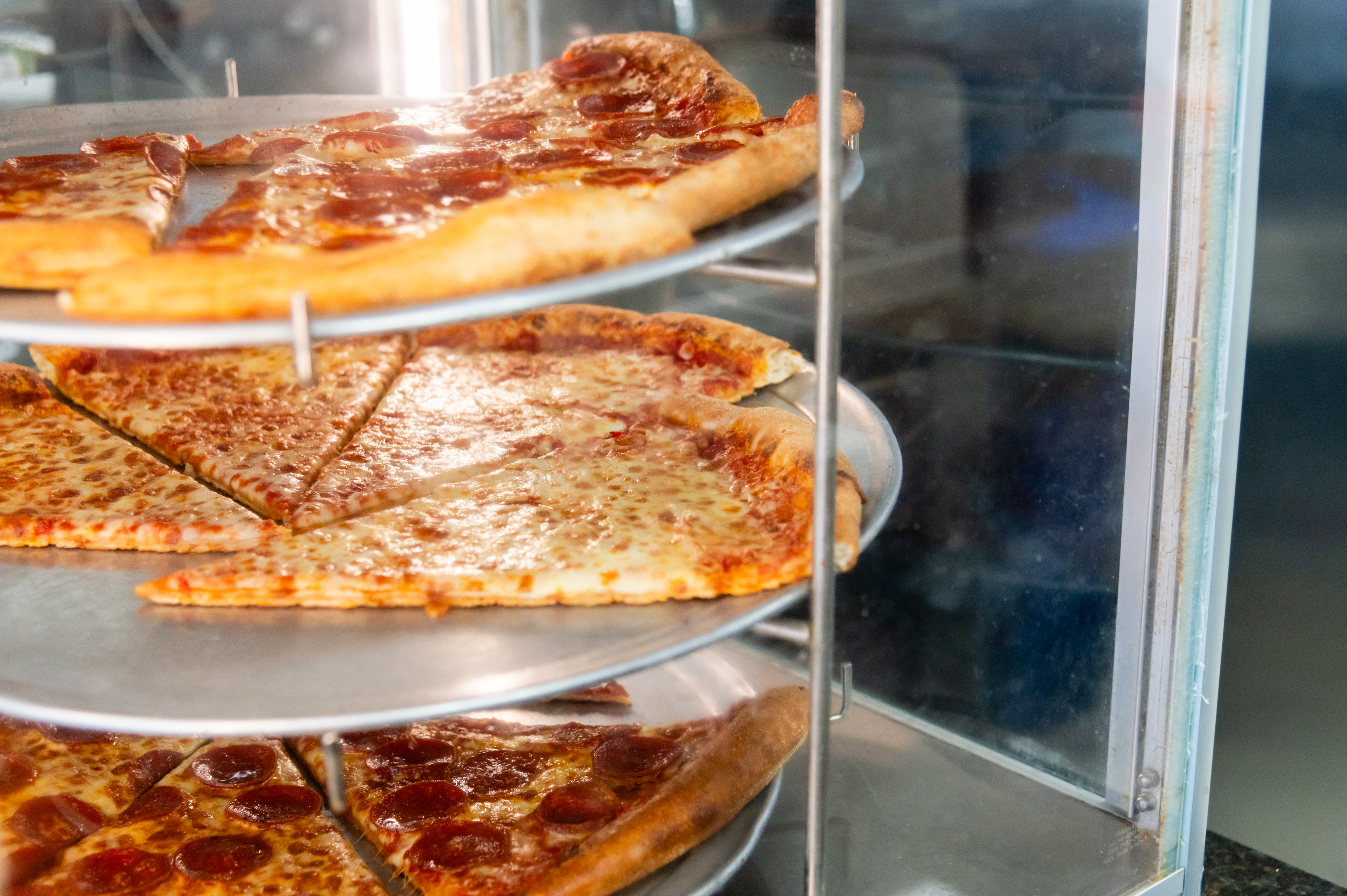 Fresh cheese and pepperoni pizza slices warming inside a glass display case at Manny & Olga’s restaurant.