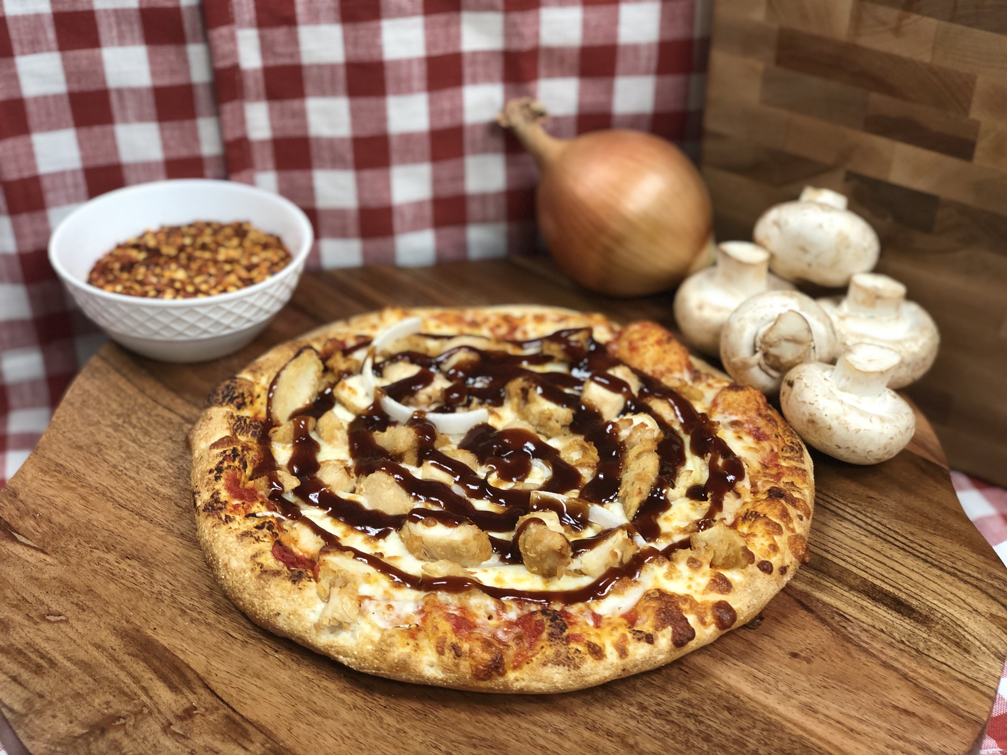 BBQ chicken pizza topped with mushrooms, onions, melted cheese, and barbecue sauce, served on a wooden board.