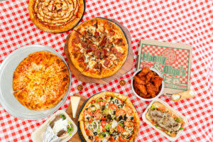 Manny & Olga's pizza feast with wings, gyro, cheesesteak, and cannoli served on a red checkered table for corporate catering.
