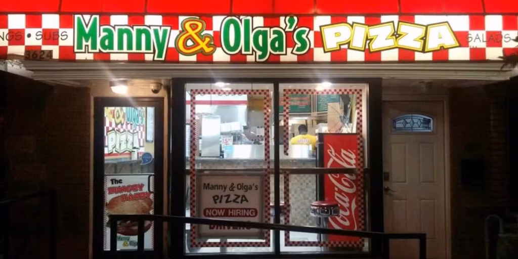 Manny & Olga's Pizza storefront illuminated at night with its signature red checkered signage, offering late-night pickup and delivery.