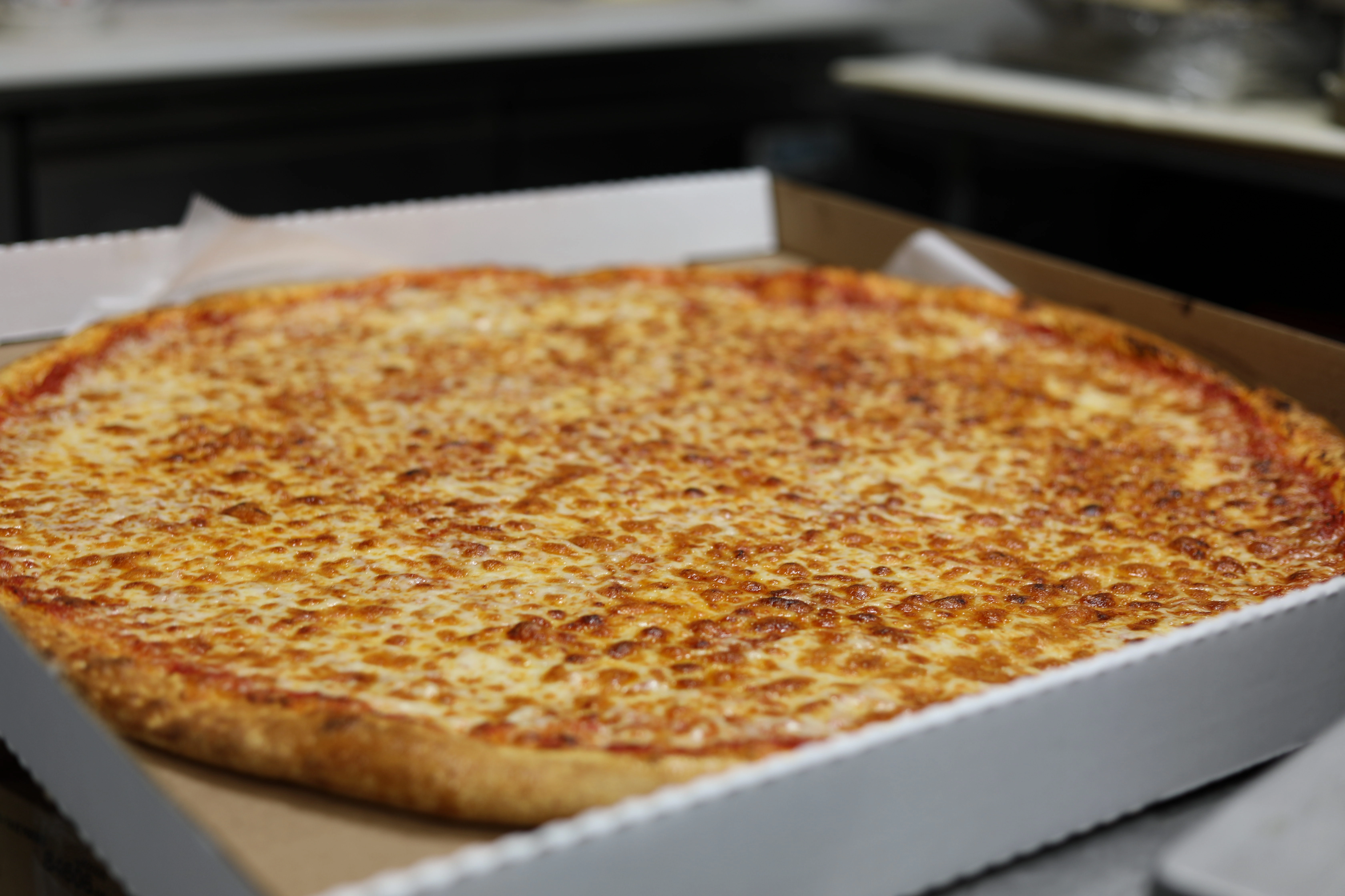 Manny & Olga's hot cheese pizza served in an open takeout box.
