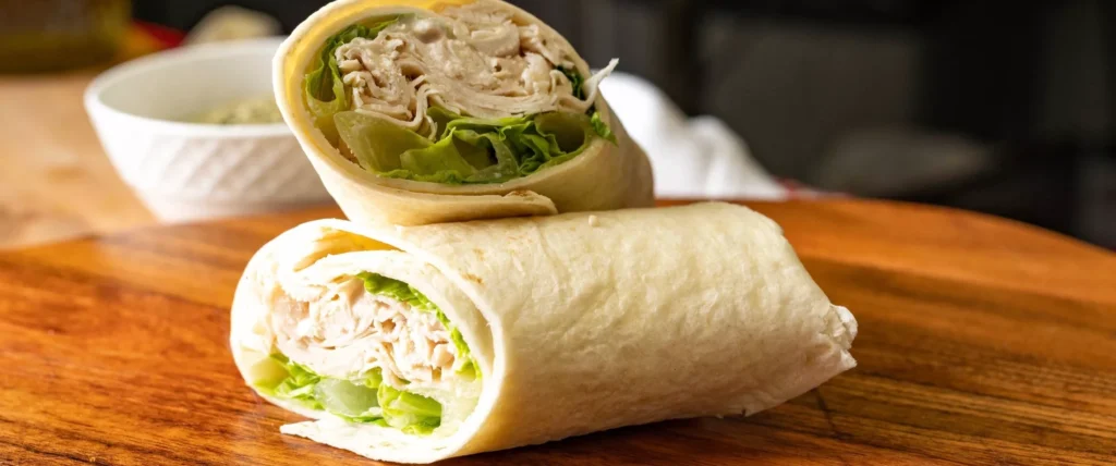 Grilled chicken wrap with fresh lettuce served on a wooden table at Manny & Olga's.