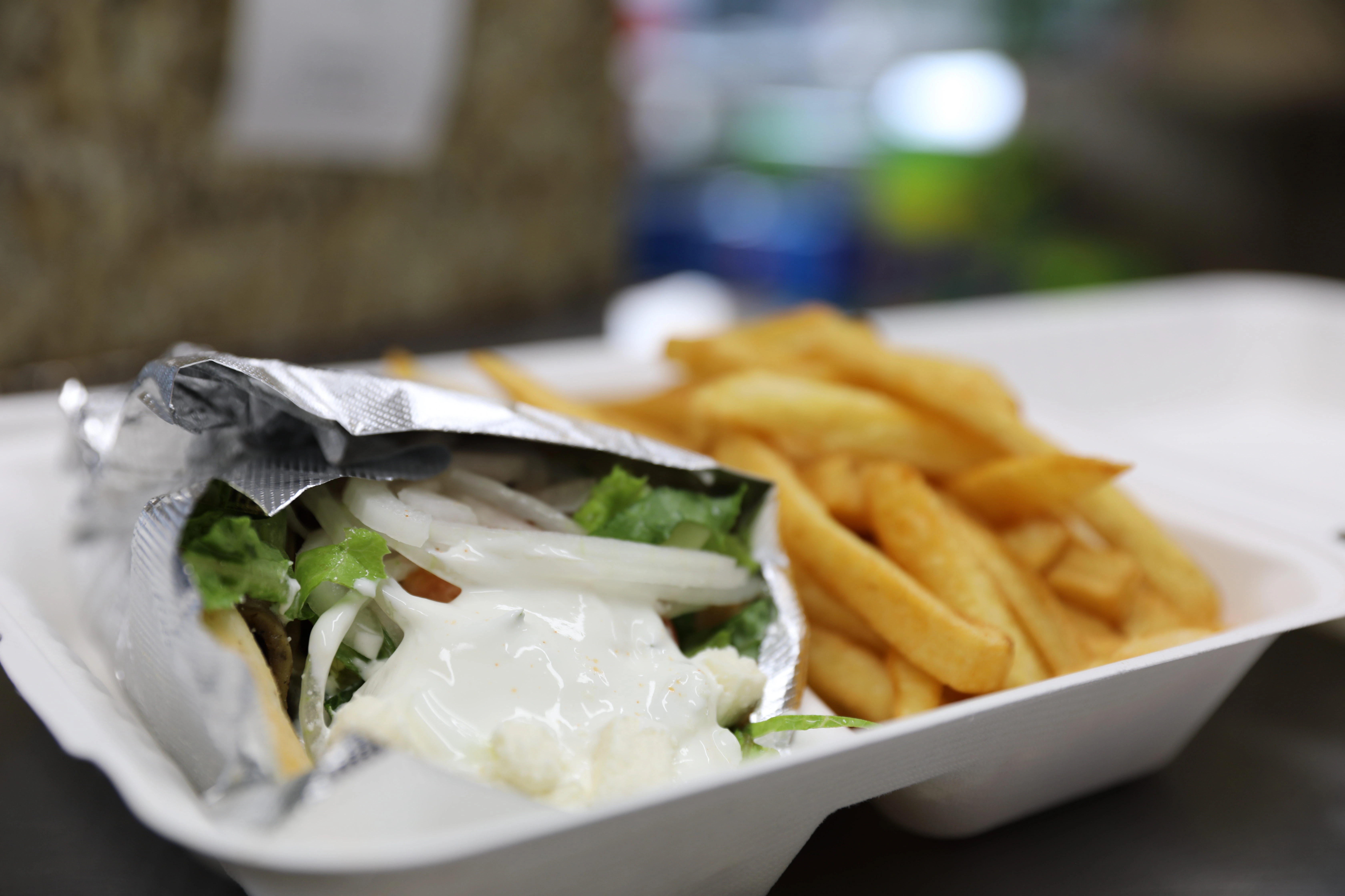 Manny & Olga's gyro with onions, lettuce, sauce, and fries in a takeout tray.