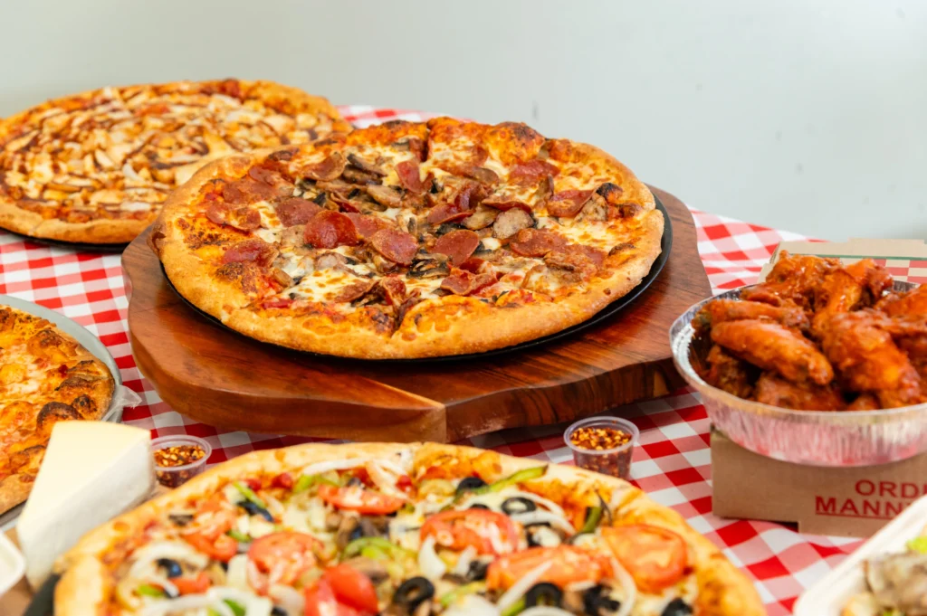 Manny & Olga's pizza and wings spread with veggie pizza, cheese pizza, and cheesecake.