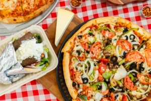 Manny & Olga’s veggie pizza and gyro served on a red checkered table.