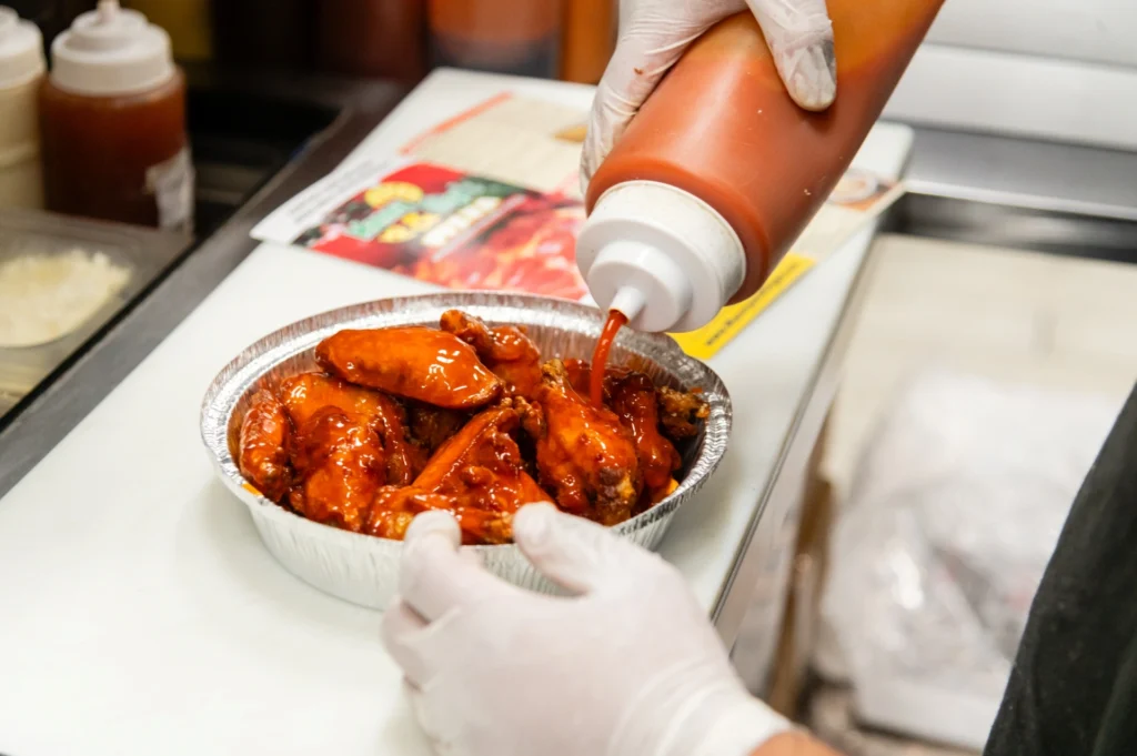 Manny & Olga’s team member coating chicken wings with sauce in the kitchen.
