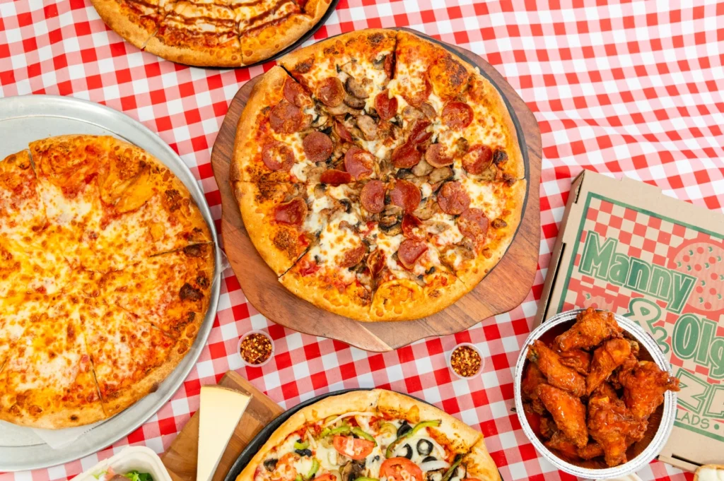 Manny & Olga’s spread with pepperoni, cheese, and veggie pizzas alongside sauced wings.