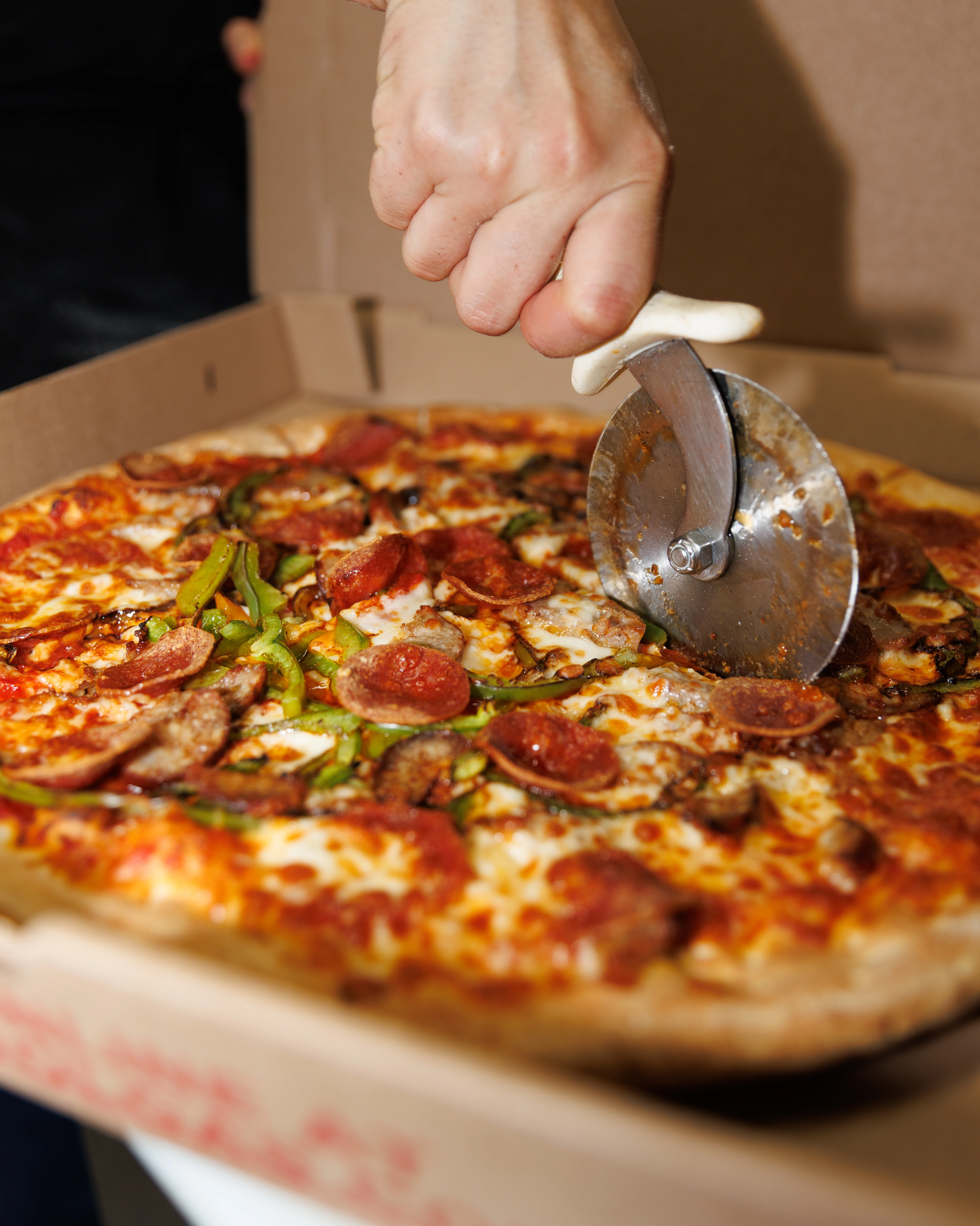 Manny & Olga’s pizza topped with pepperoni, sausage, green peppers, and cheese being sliced.
