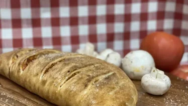 Golden baked calzone on wooden board with fresh mushrooms and tomato at Manny & Olga’s.