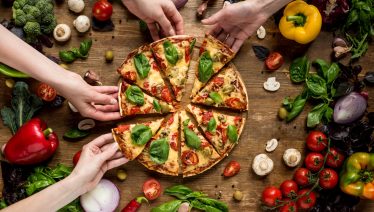 A group of friends enjoy slices of veggie pizza at a National Pizza Party Day celebration.
